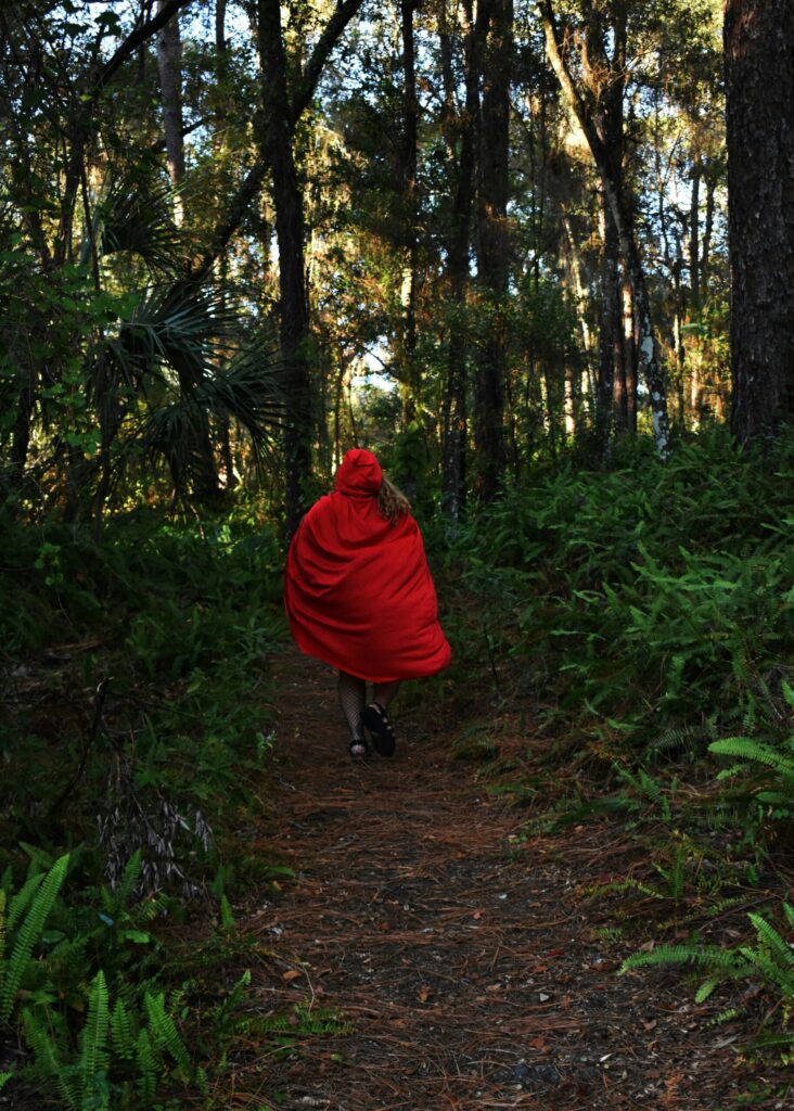 Little Red Riding Hood skipping away down a path in a thick forest.